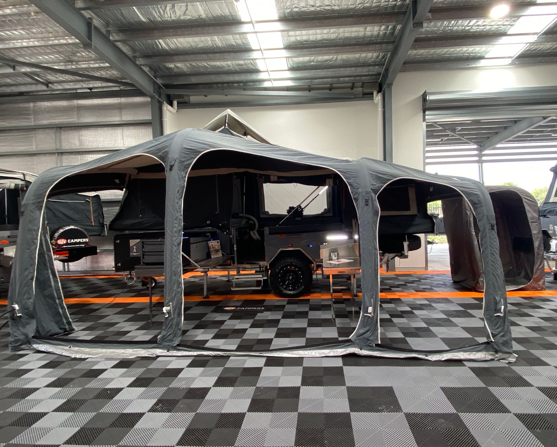 A tent is sitting on top of a checkered floor next to a trailer.