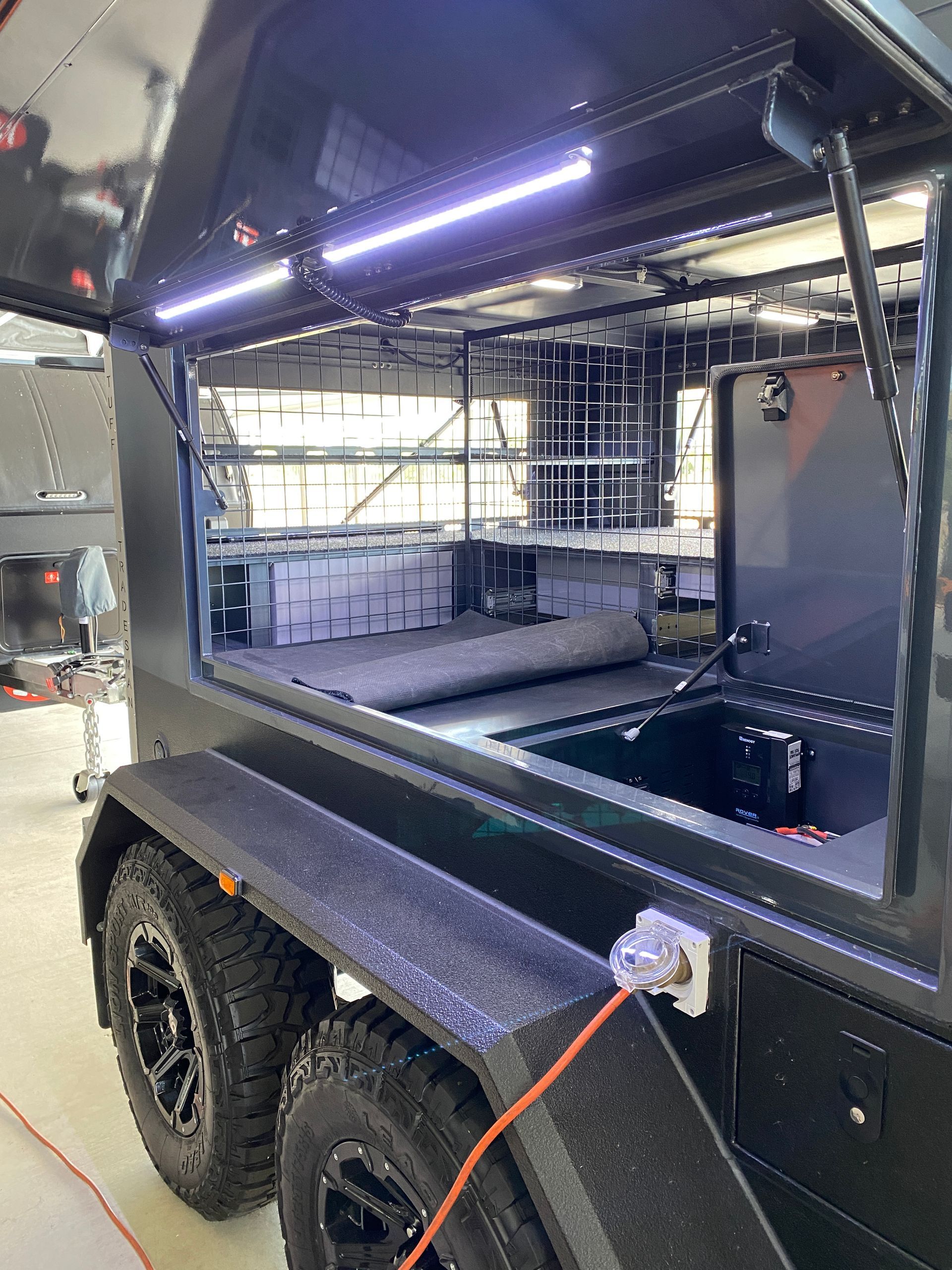 A black trailer with a canopy on top of it is sitting in a garage.