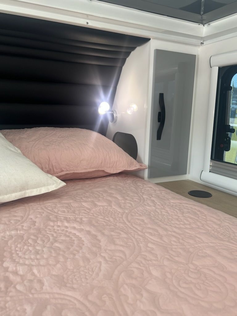 A bed with pink sheets and pillows in a camper van.