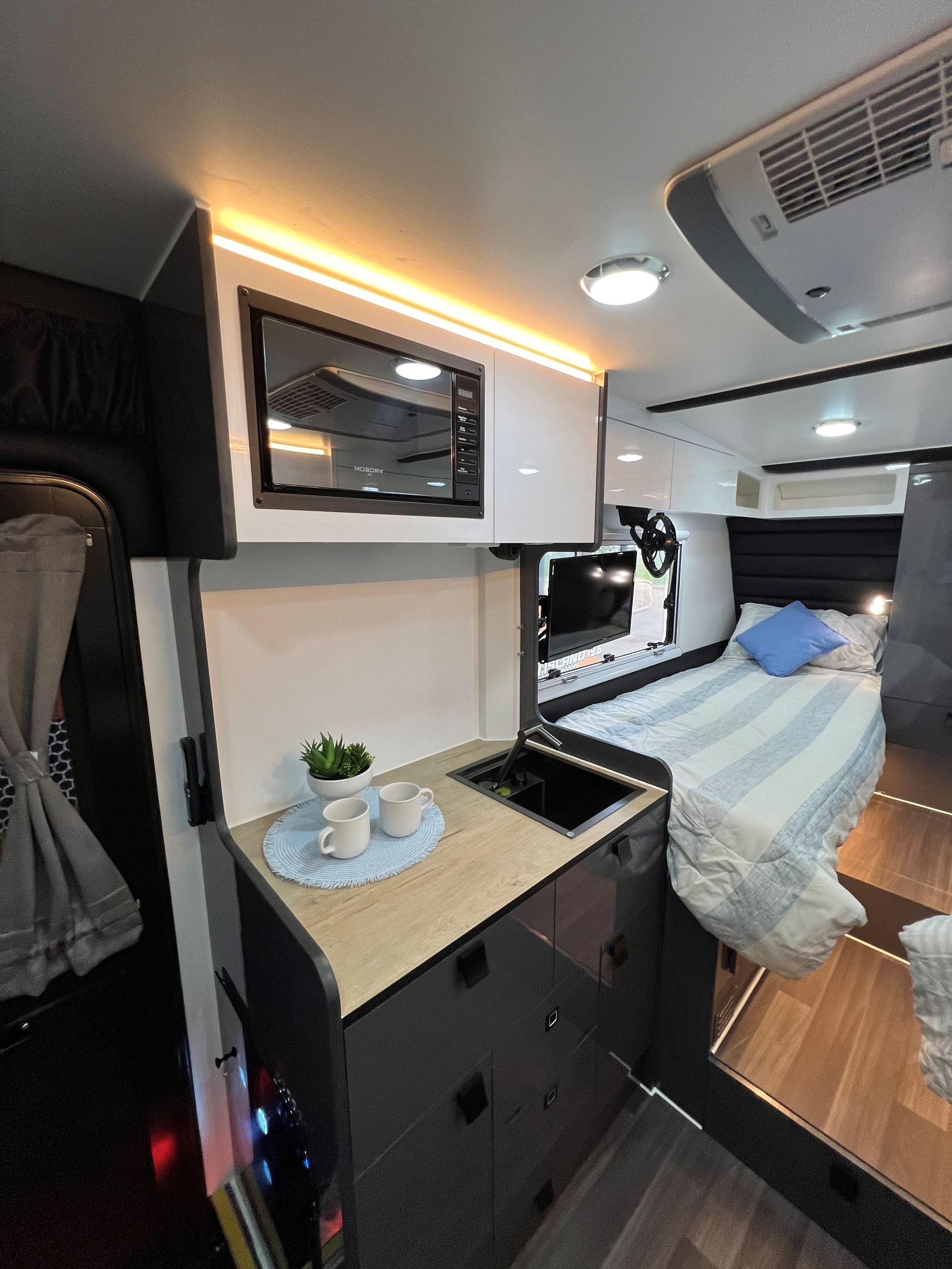 A kitchen with a sink , microwave , and bed in a camper van.