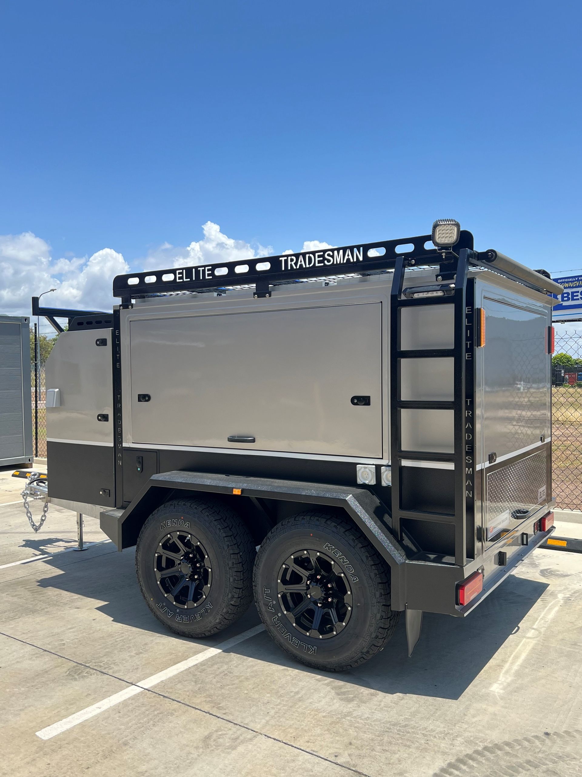 A trailer with a ladder on the back is parked in a parking lot.
