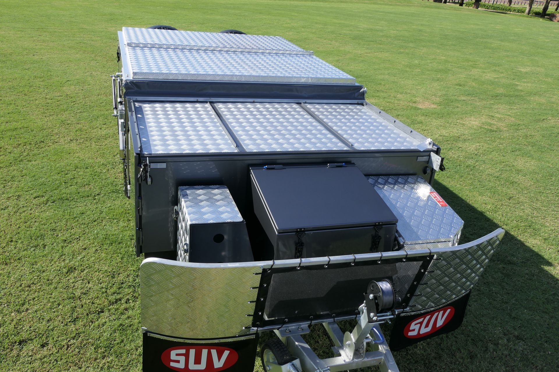 A suv trailer is parked in a grassy field.