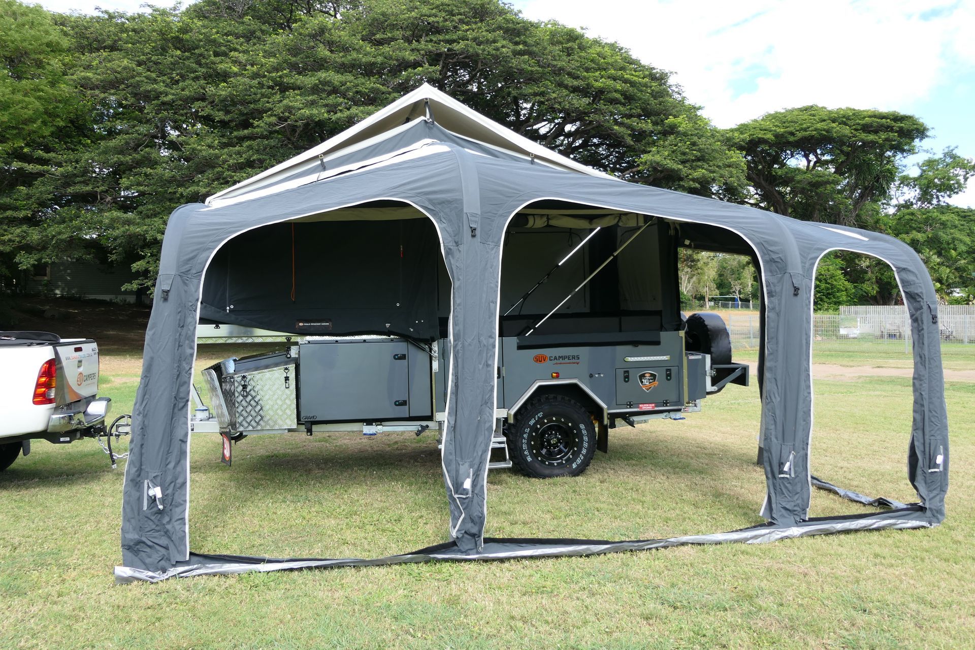 A trailer with a tent attached to it is parked in a grassy field.