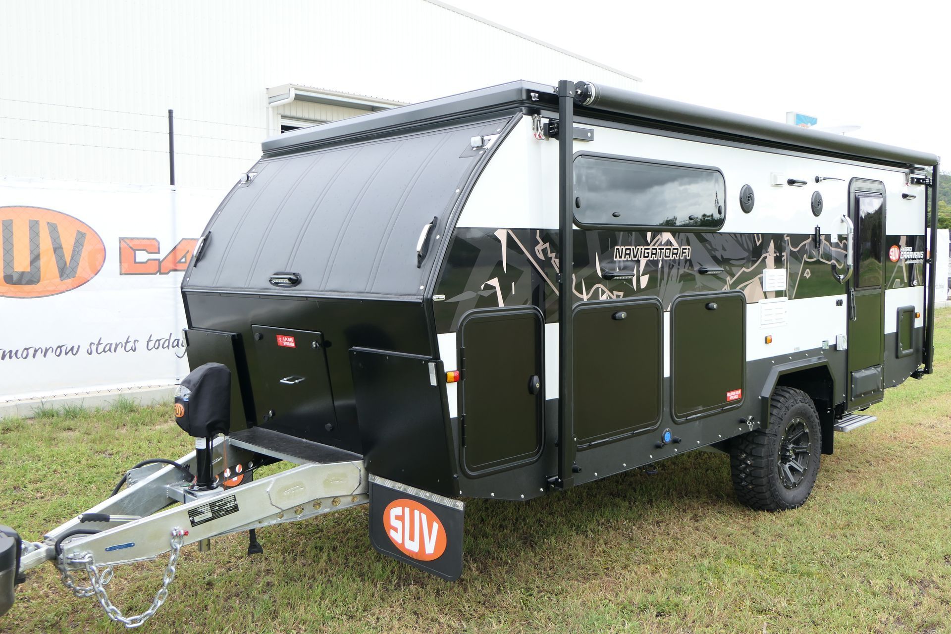 A black and white trailer is parked in the grass in front of a building.