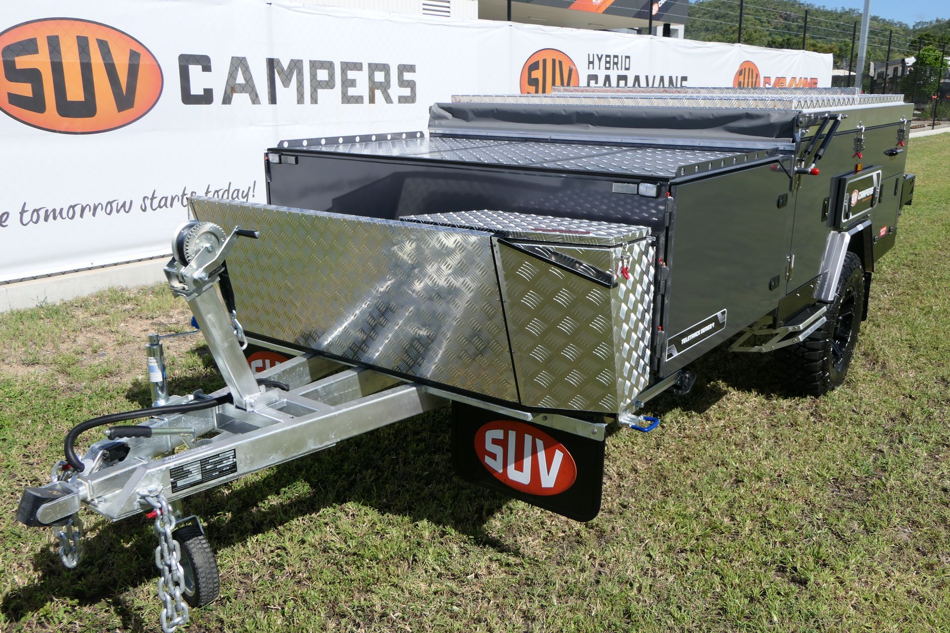 A silver trailer is parked in the grass in front of a suv campers sign.
