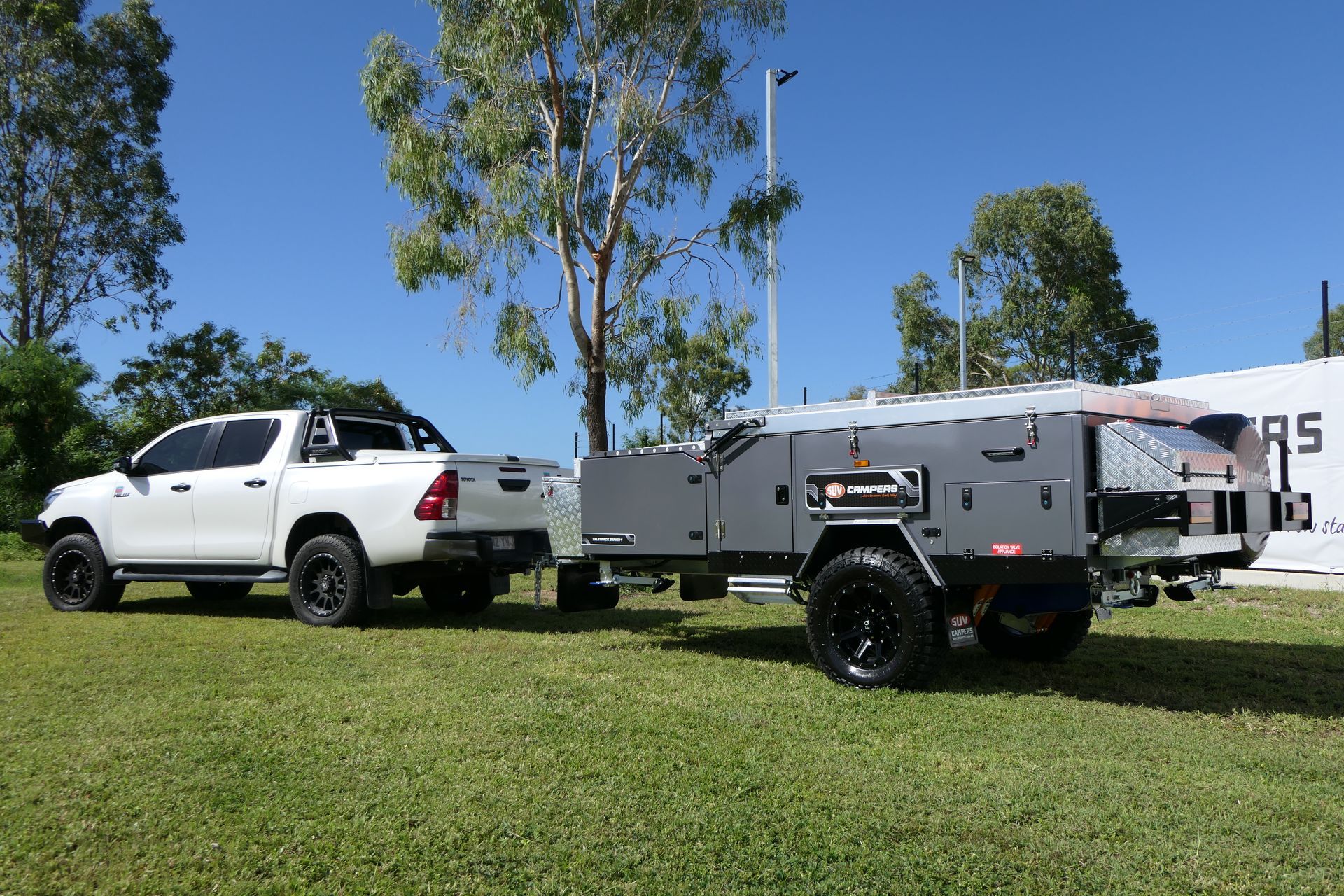 A white truck is towing a trailer in a grassy field.