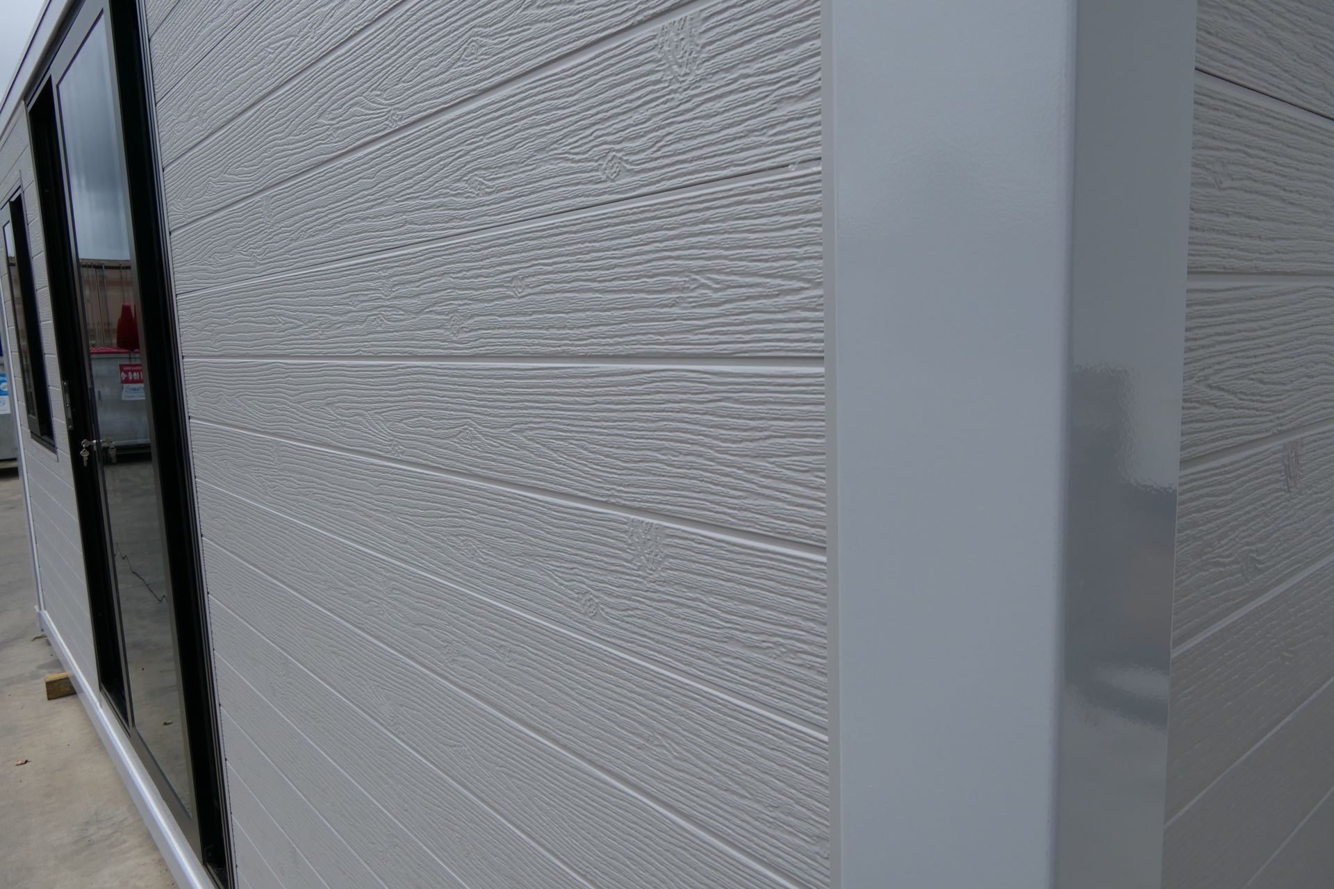 A close up of the side of a building with a gray siding and black windows.