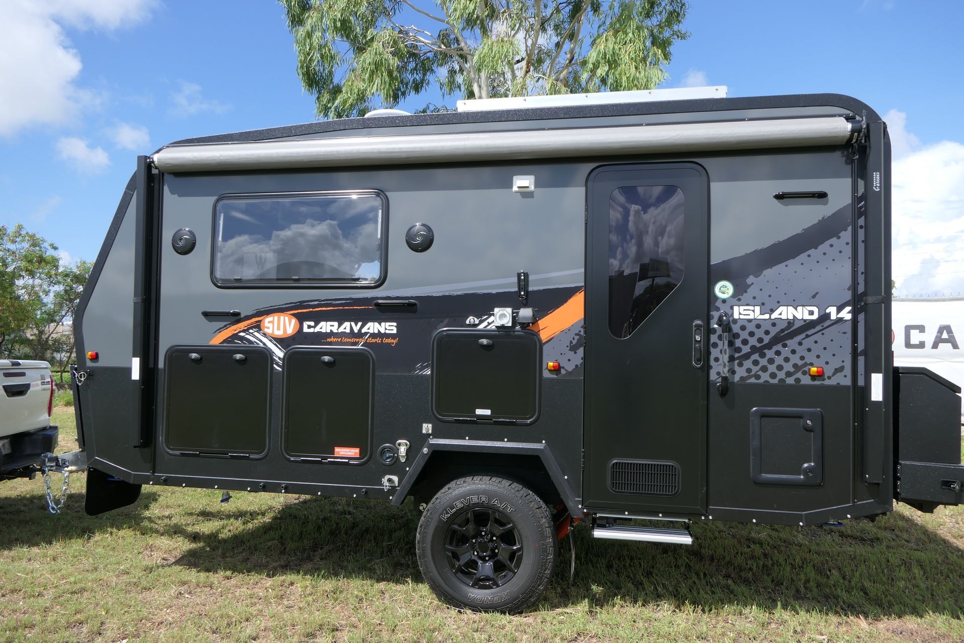 A black trailer is parked in a grassy field next to a truck.