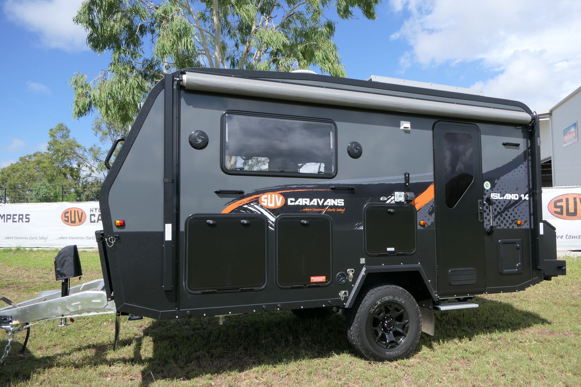 A black camper trailer is parked in a grassy field.