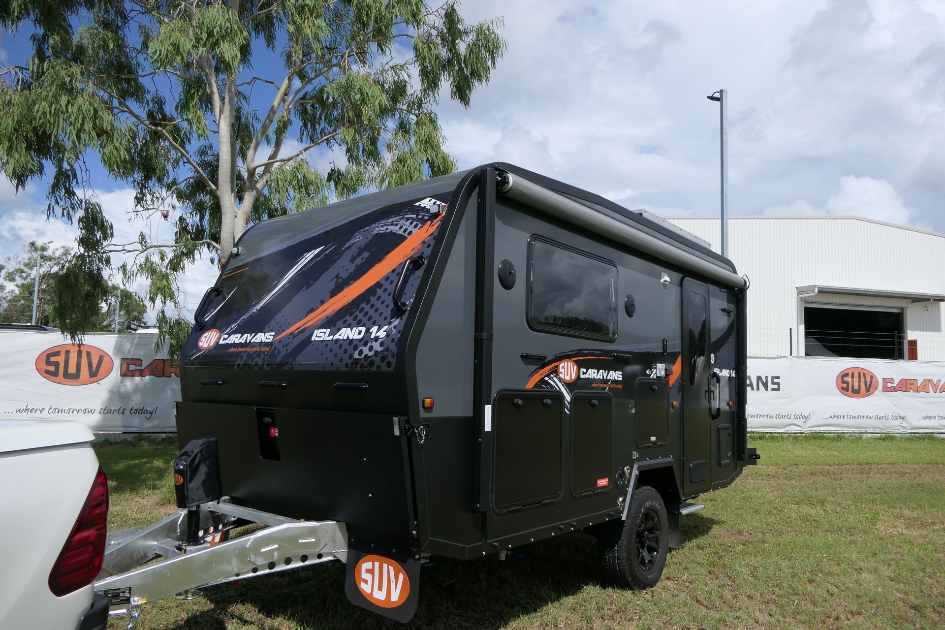 A black camper trailer is parked in the grass in front of a building.