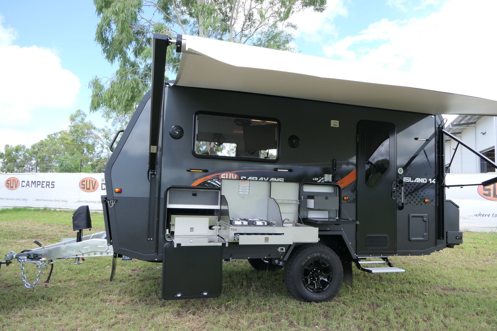 A black trailer with a white awning is parked in a grassy field.