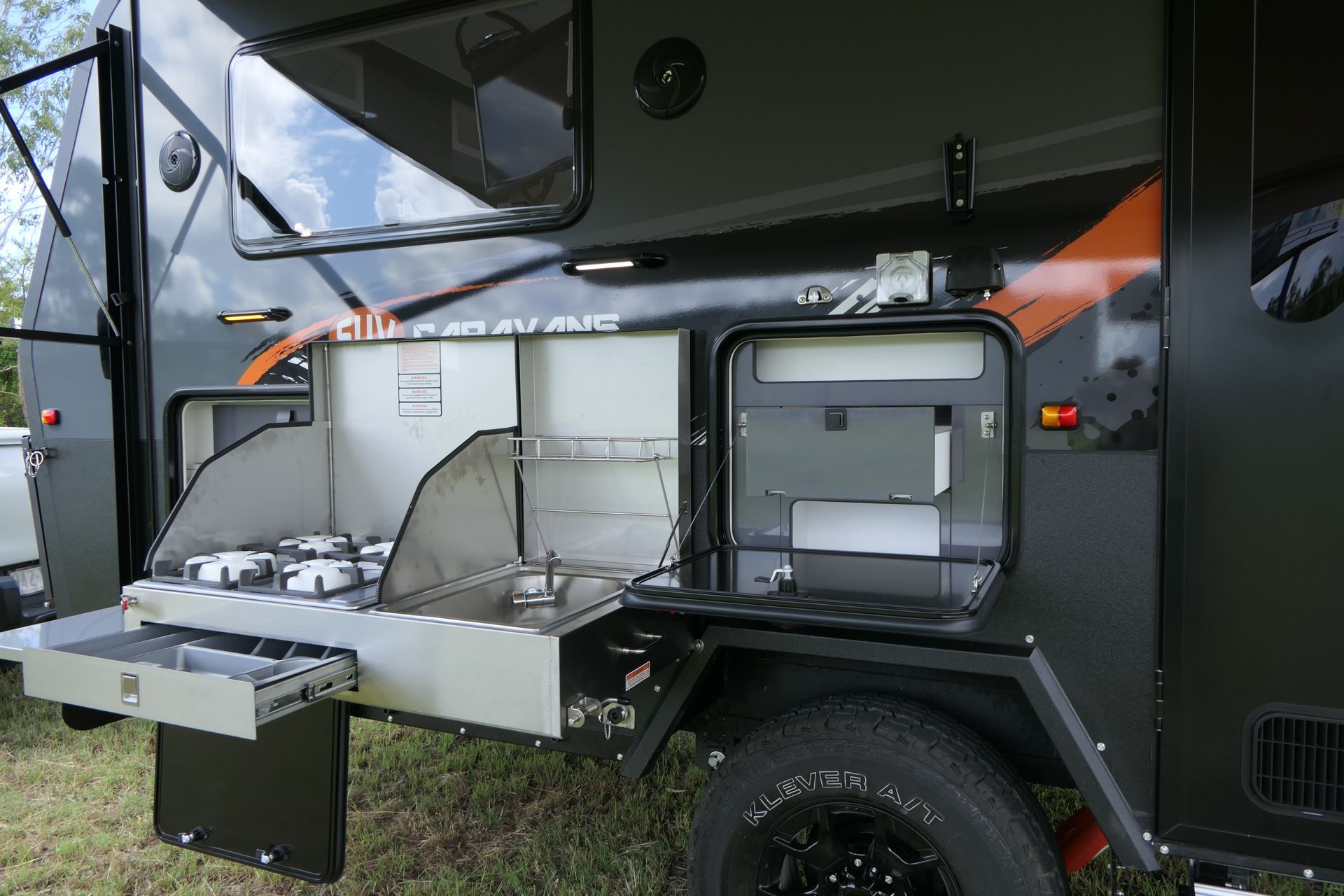 A trailer with a kitchen attached to it is parked in the grass.