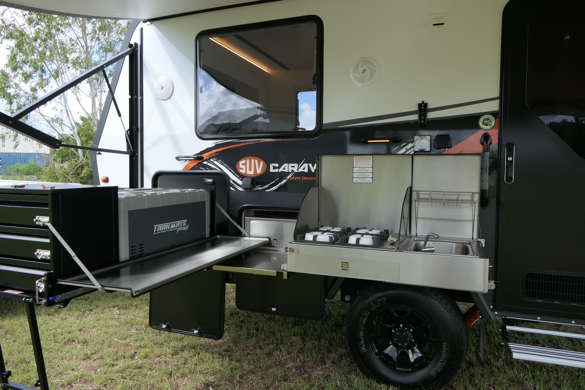 A trailer with a kitchen attached to it is parked in the grass.
