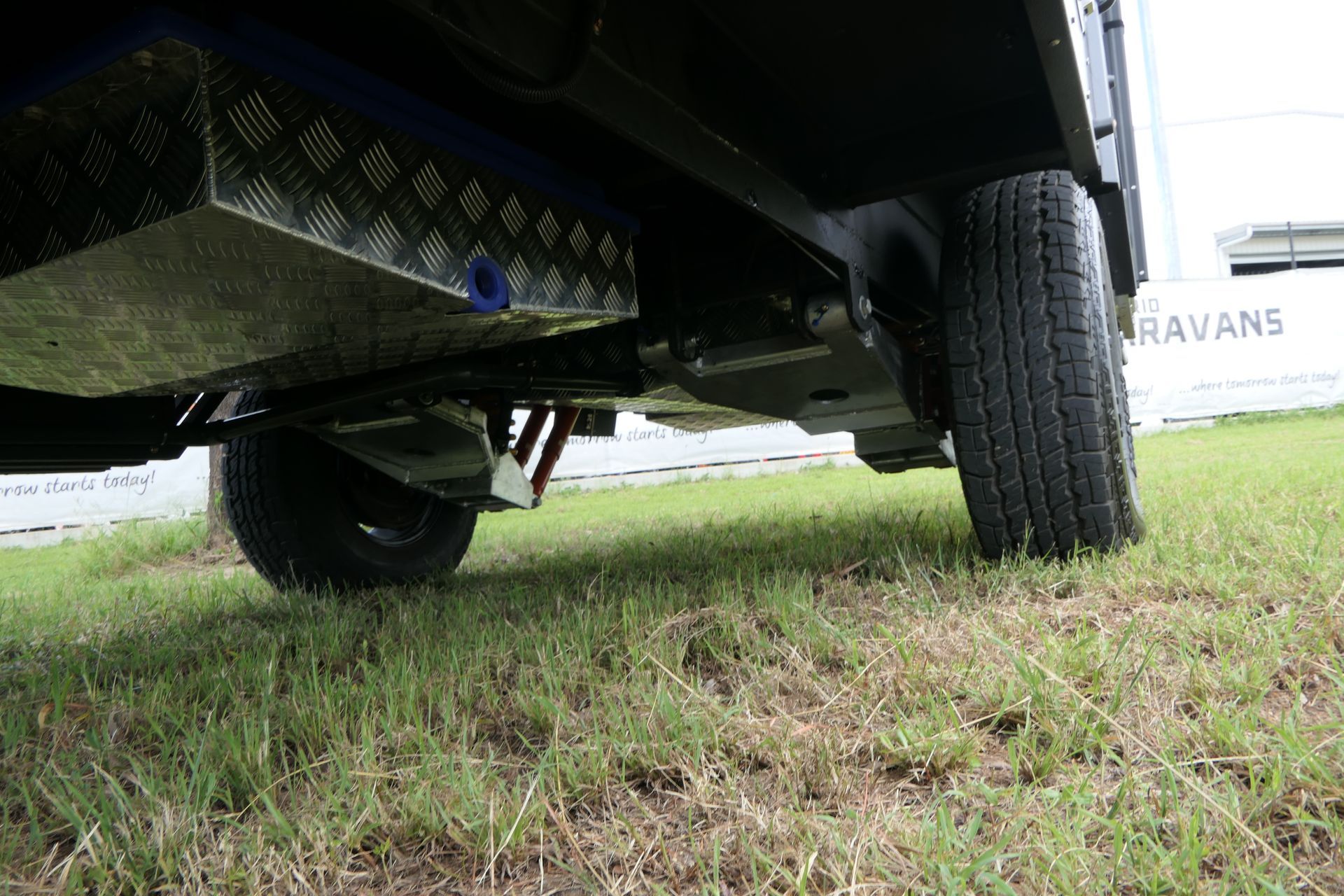 Undercarriage view of a vehicle with a metal storage tank and tires on grass.