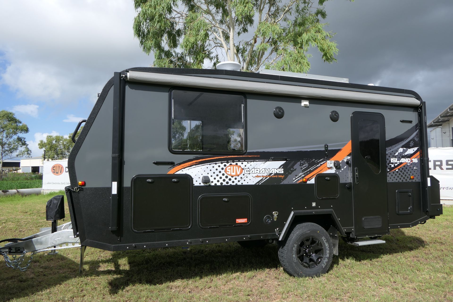 A black and orange camper trailer is parked in a grassy field.