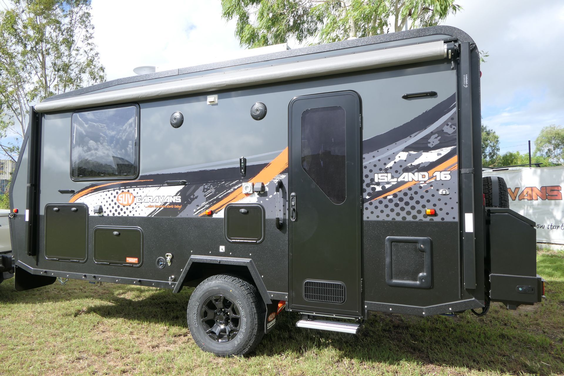 Dark gray caravan with black wheels, awning, and door, parked on grass.