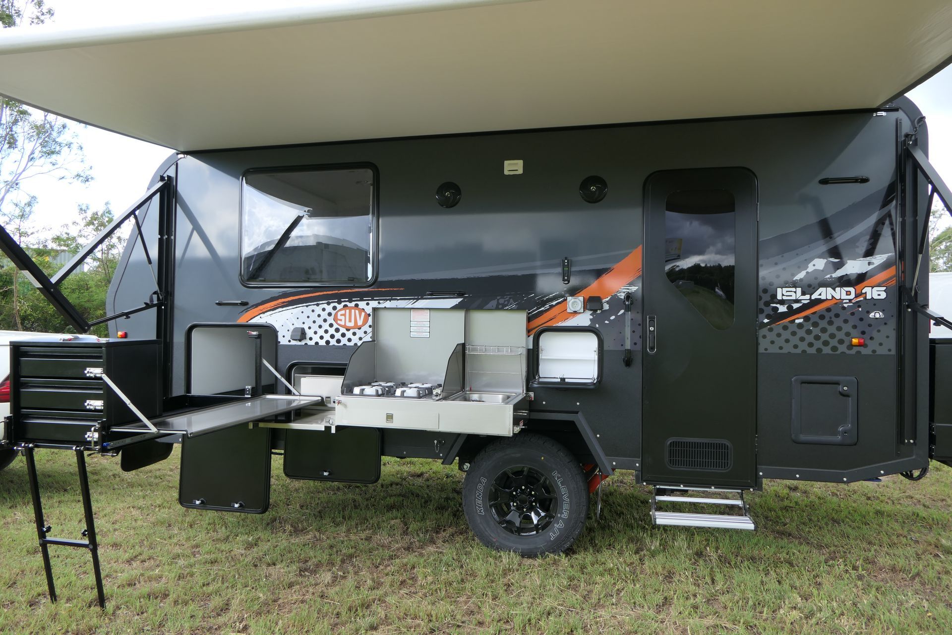 A black camper trailer is parked in a grassy field.