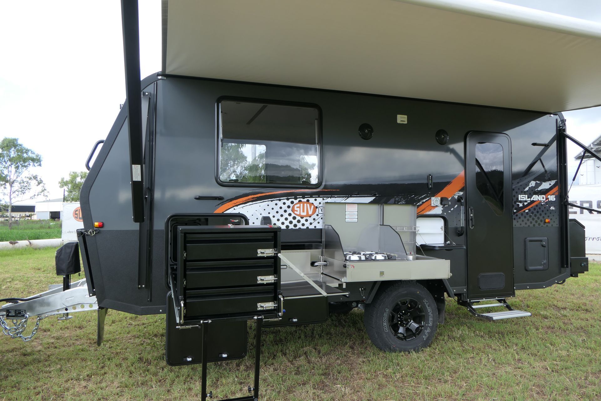 Dark gray camper with awning extended. Outdoor kitchen and storage compartment visible.