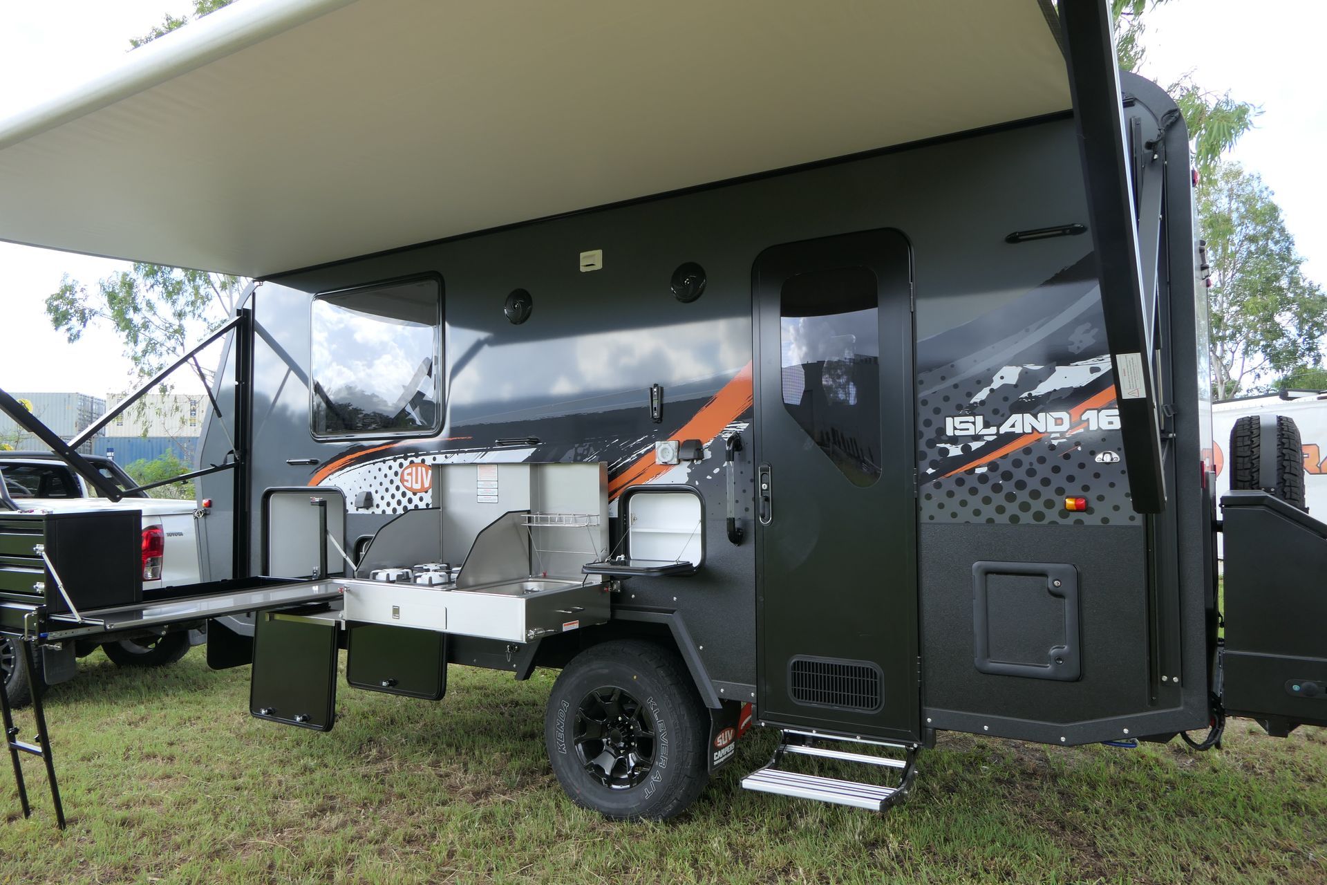 Dark green RV with an open awning and outdoor kitchen.