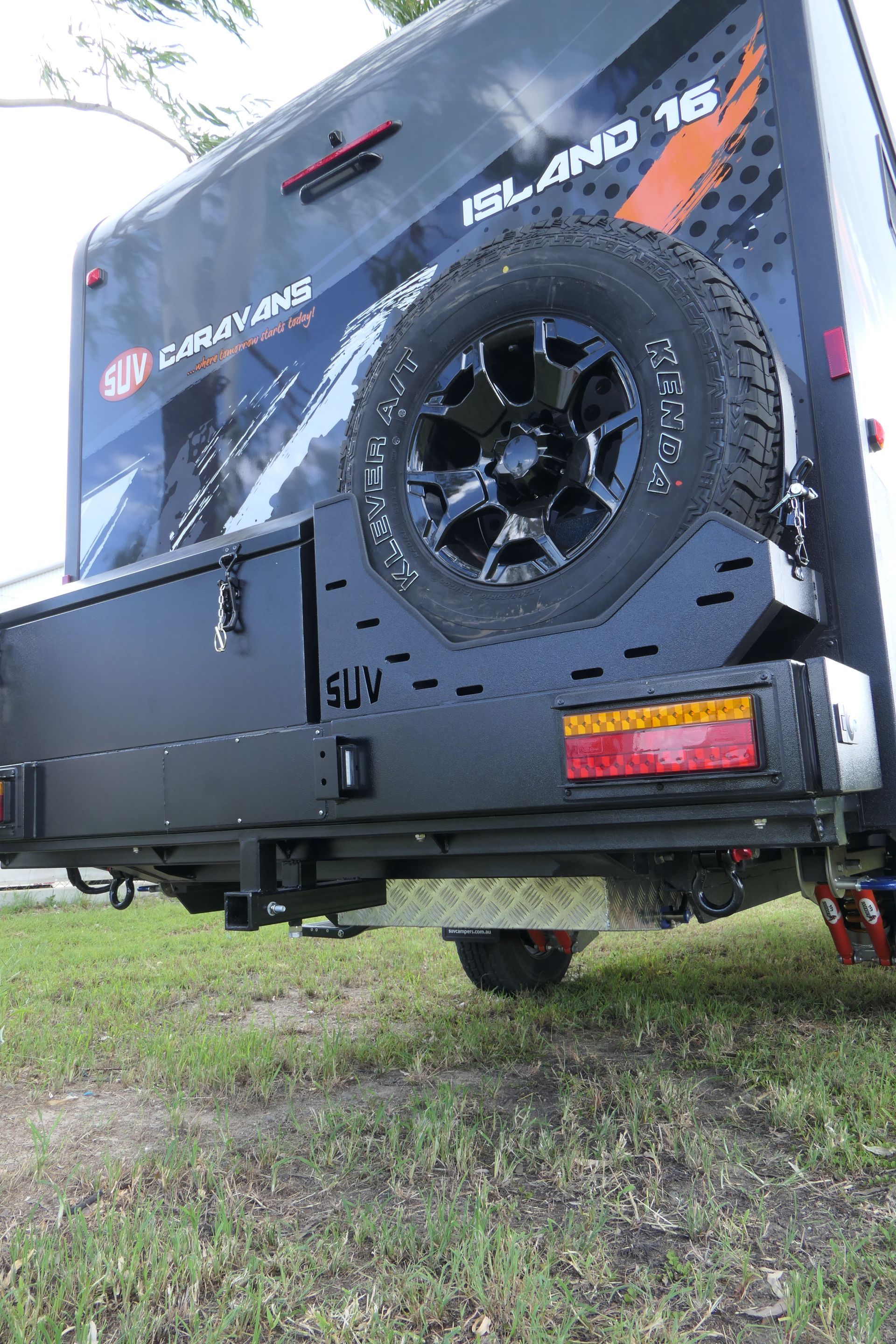 A trailer with a spare tire attached to the back of it is parked in the grass.