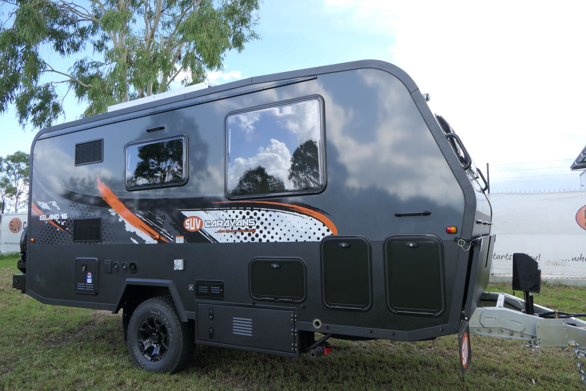 A black camper trailer is parked in a grassy field.