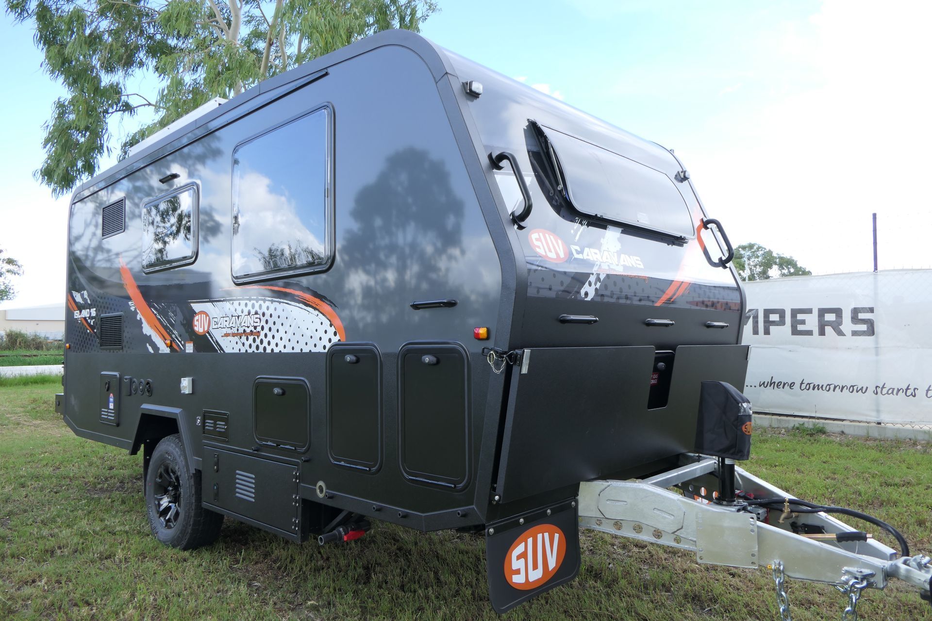 A black camper trailer is parked in a grassy field.