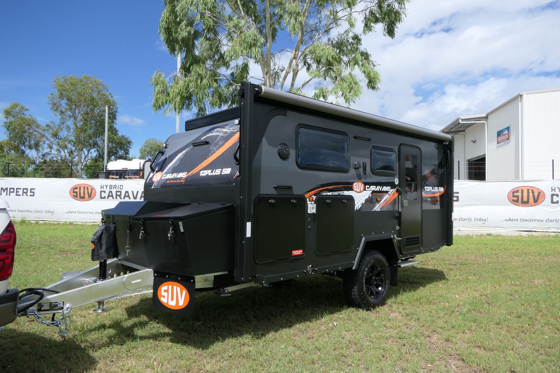 A black trailer is parked in a grassy field next to a building.