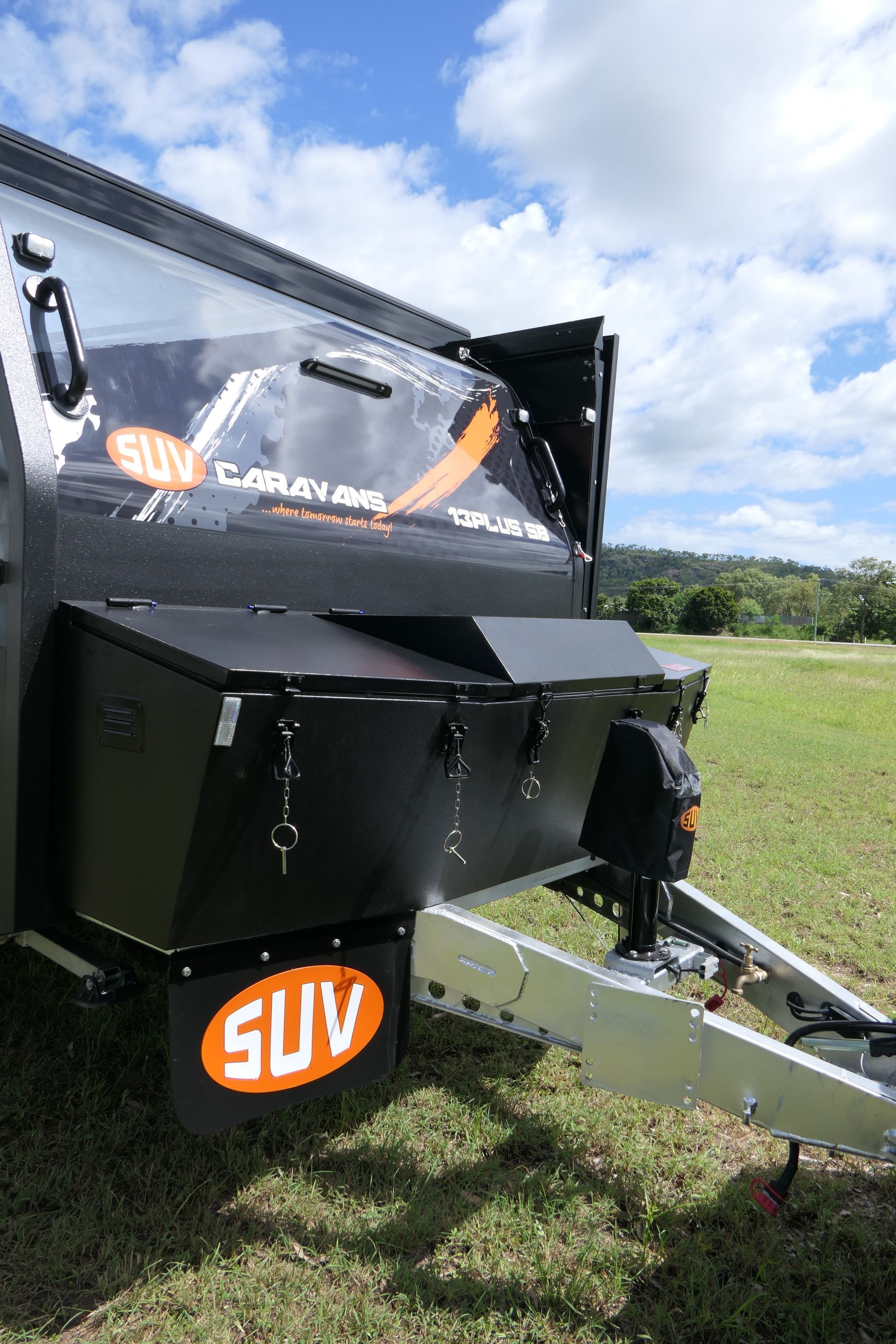 A black suv trailer is parked in a grassy field.