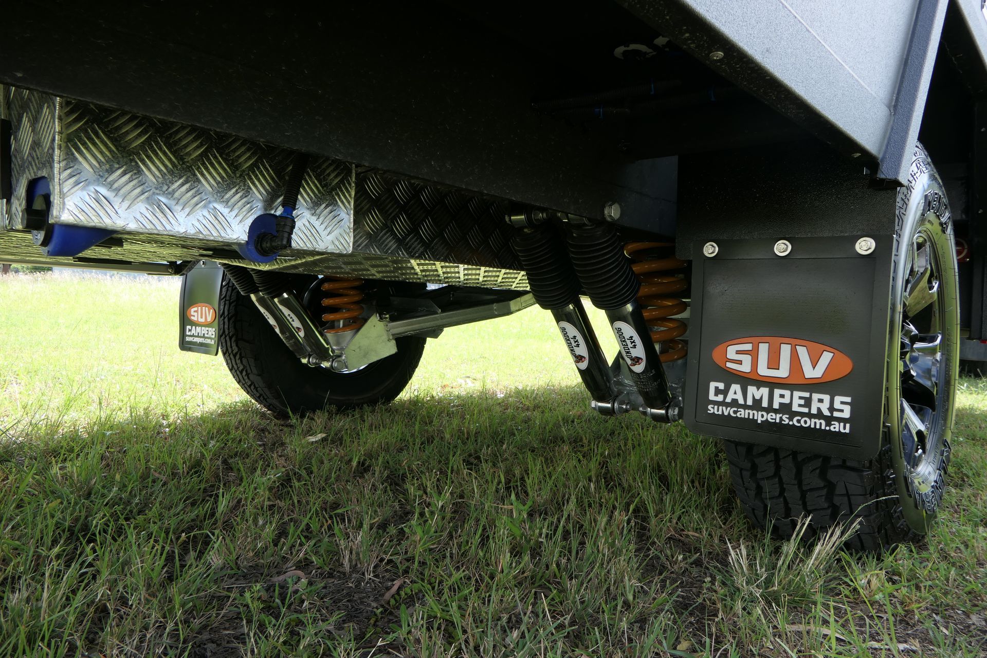 A suv is parked in the grass with mud flaps on the fenders.