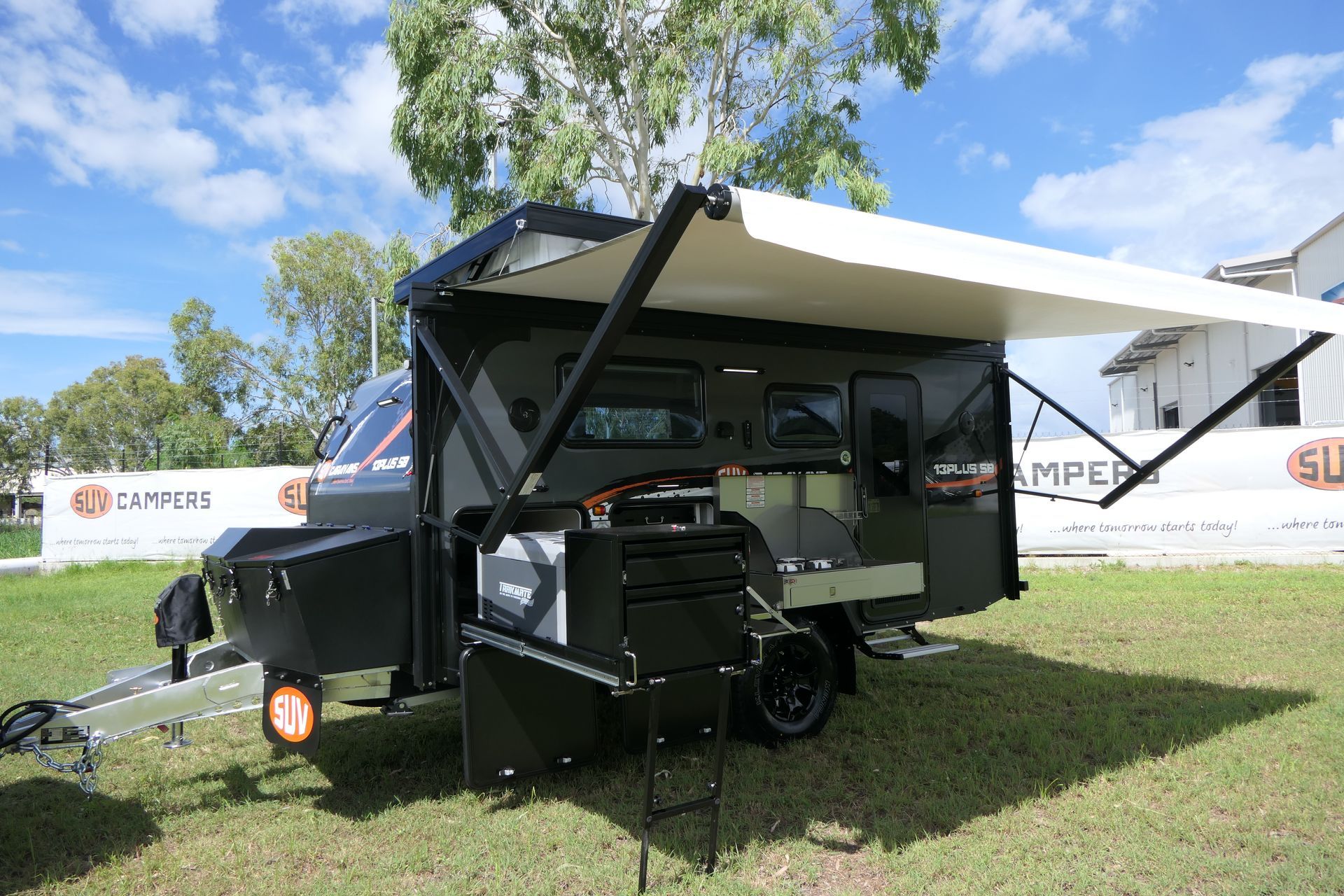 A black trailer with a white awning is parked in a grassy field.