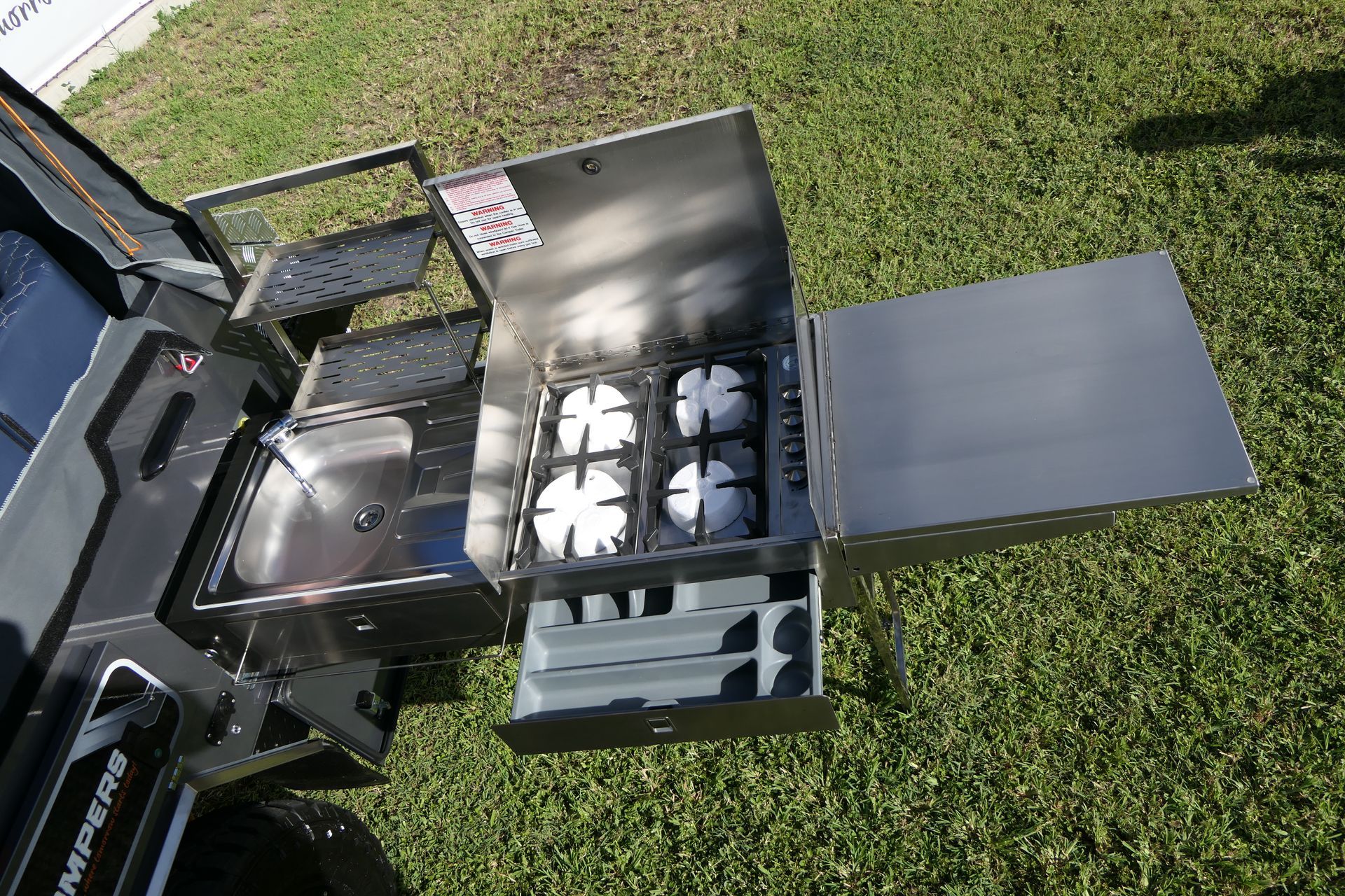 A stainless steel stove with a sink attached to it is sitting on top of a lush green field.
