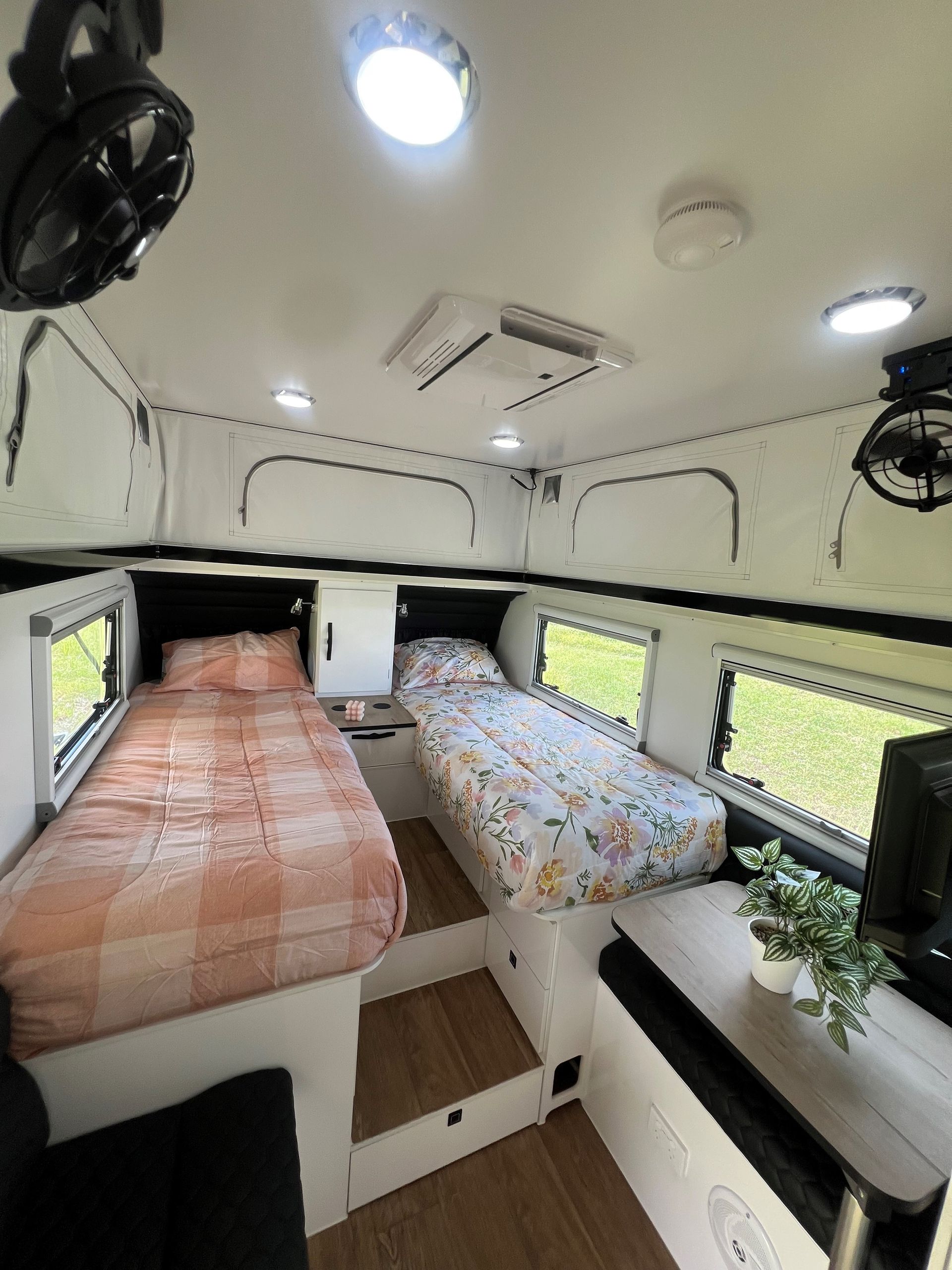 A camper with two beds and a fan on the ceiling.