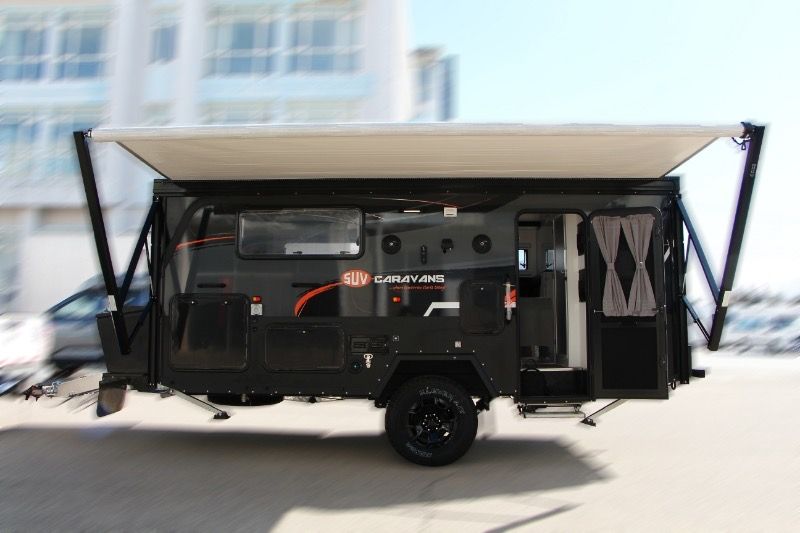 A black trailer with a white awning is parked in a parking lot.