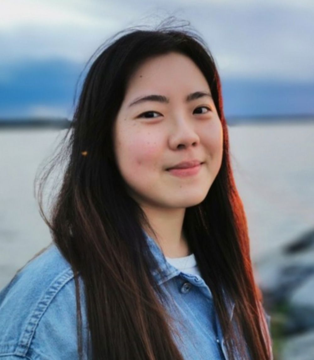 A woman with long hair is wearing a denim jacket and smiling for the camera.