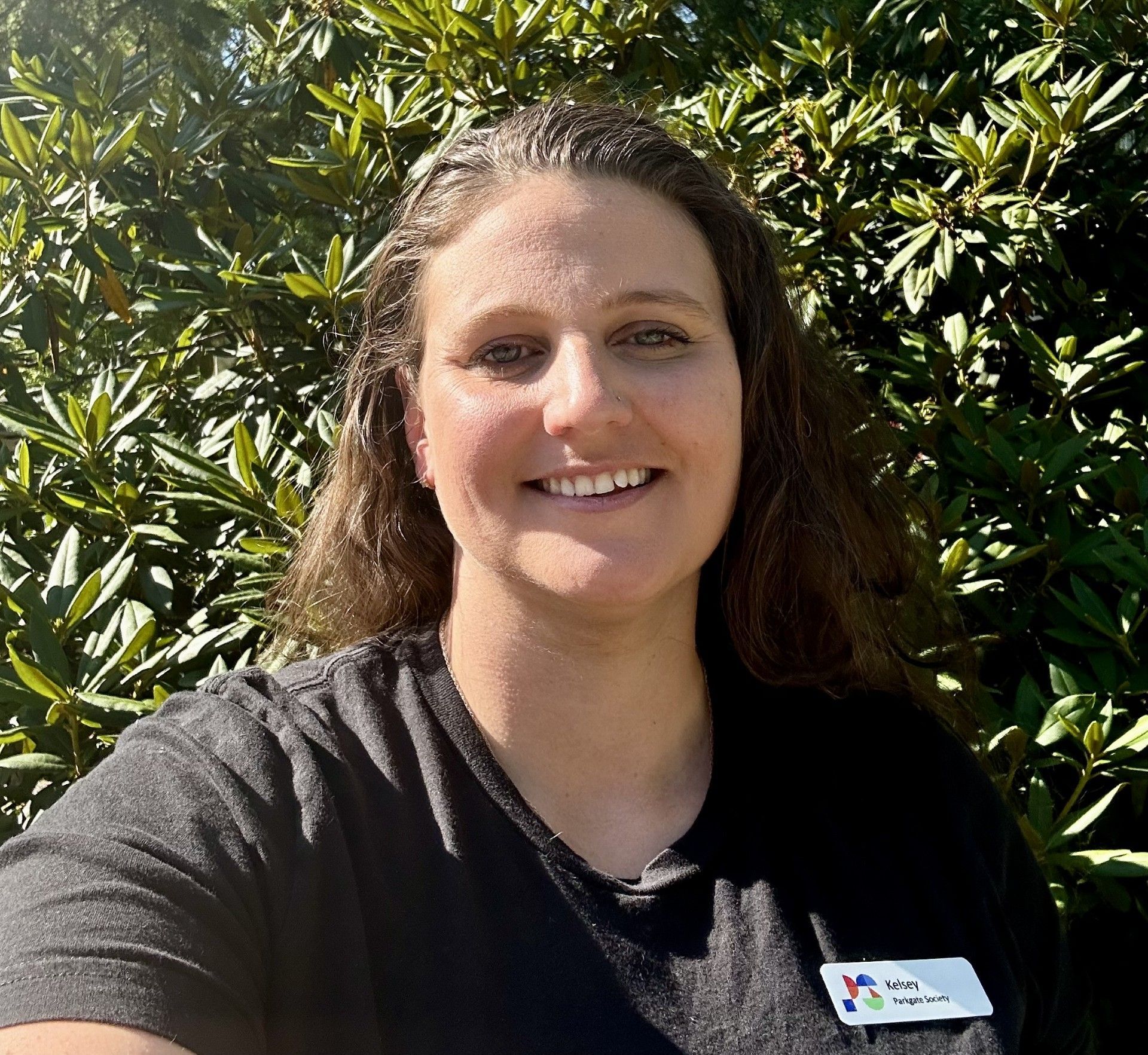 A woman in a black shirt is smiling in front of a tree.