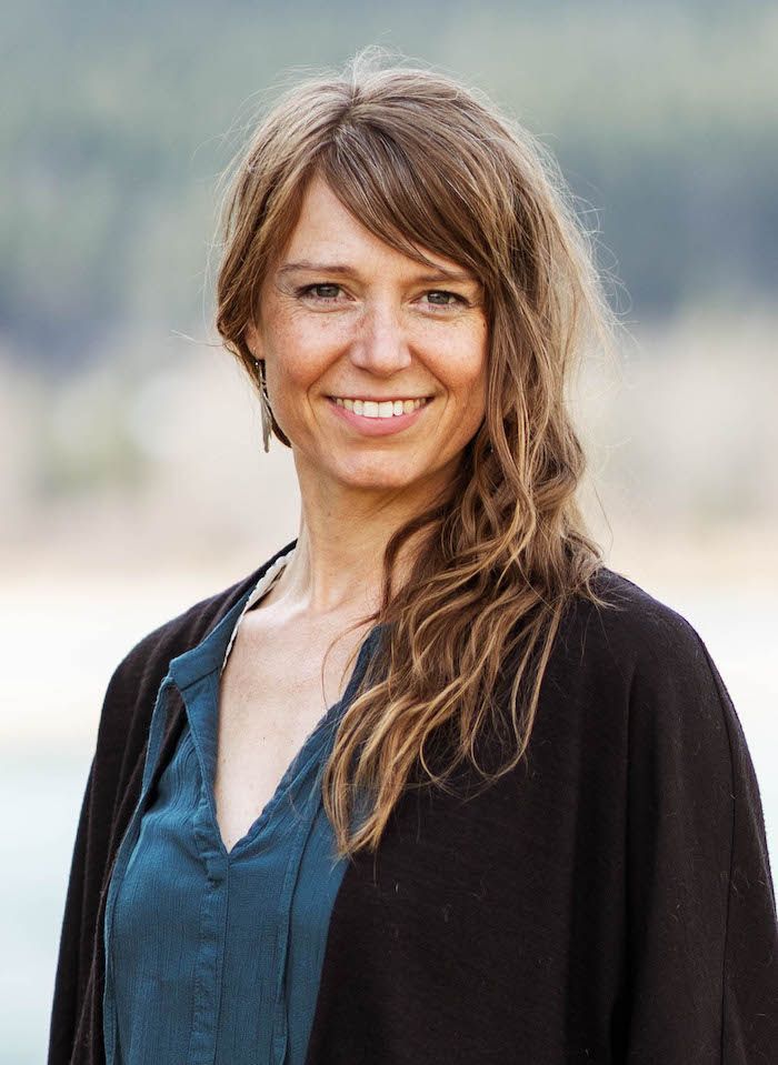 A woman wearing a black cardigan and a blue shirt is smiling for the camera.
