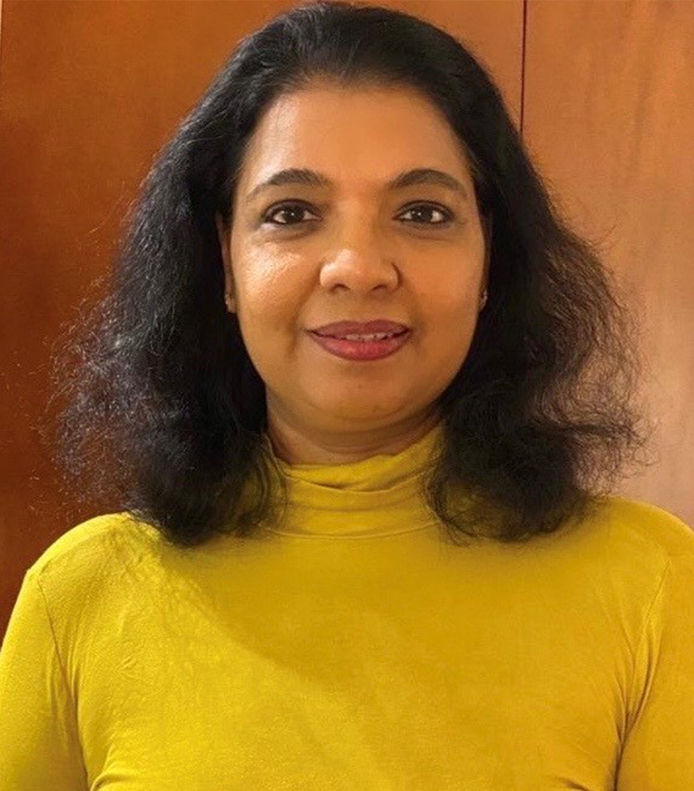 Woman in a yellow turtleneck smiling against a plain brown background