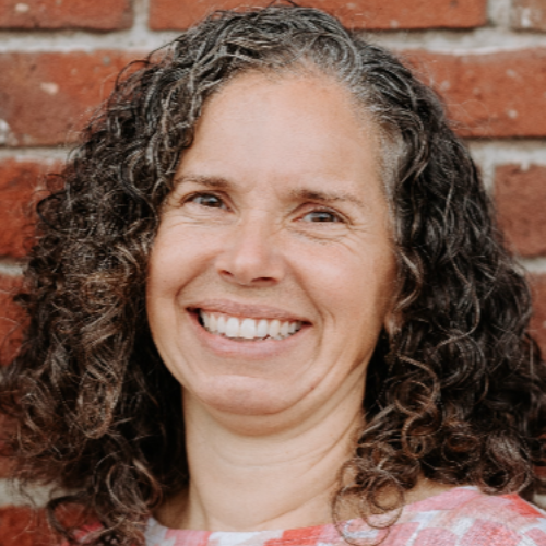 A woman with long hair and pink lipstick is wearing a black shirt.