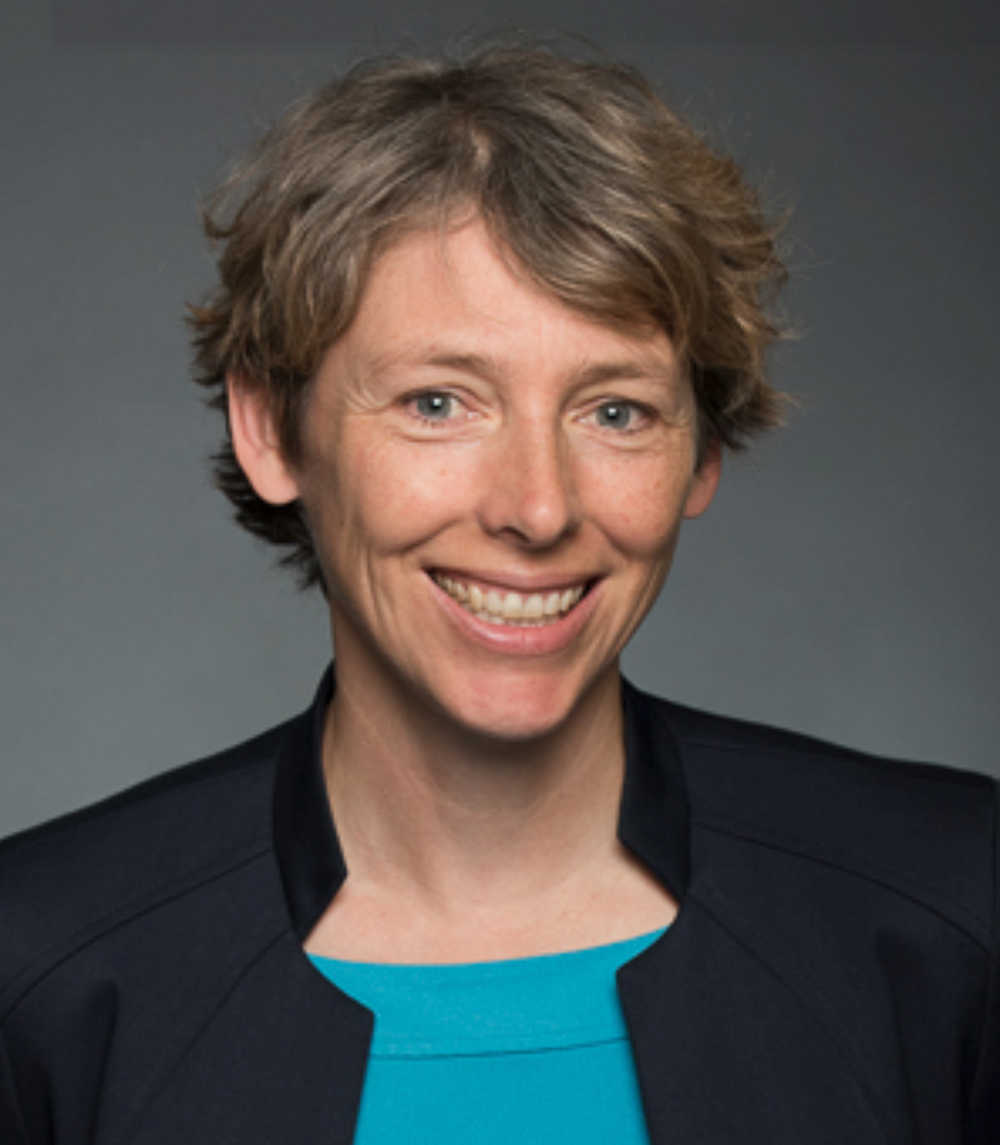 A woman wearing a blue shirt and a black jacket smiles for the camera