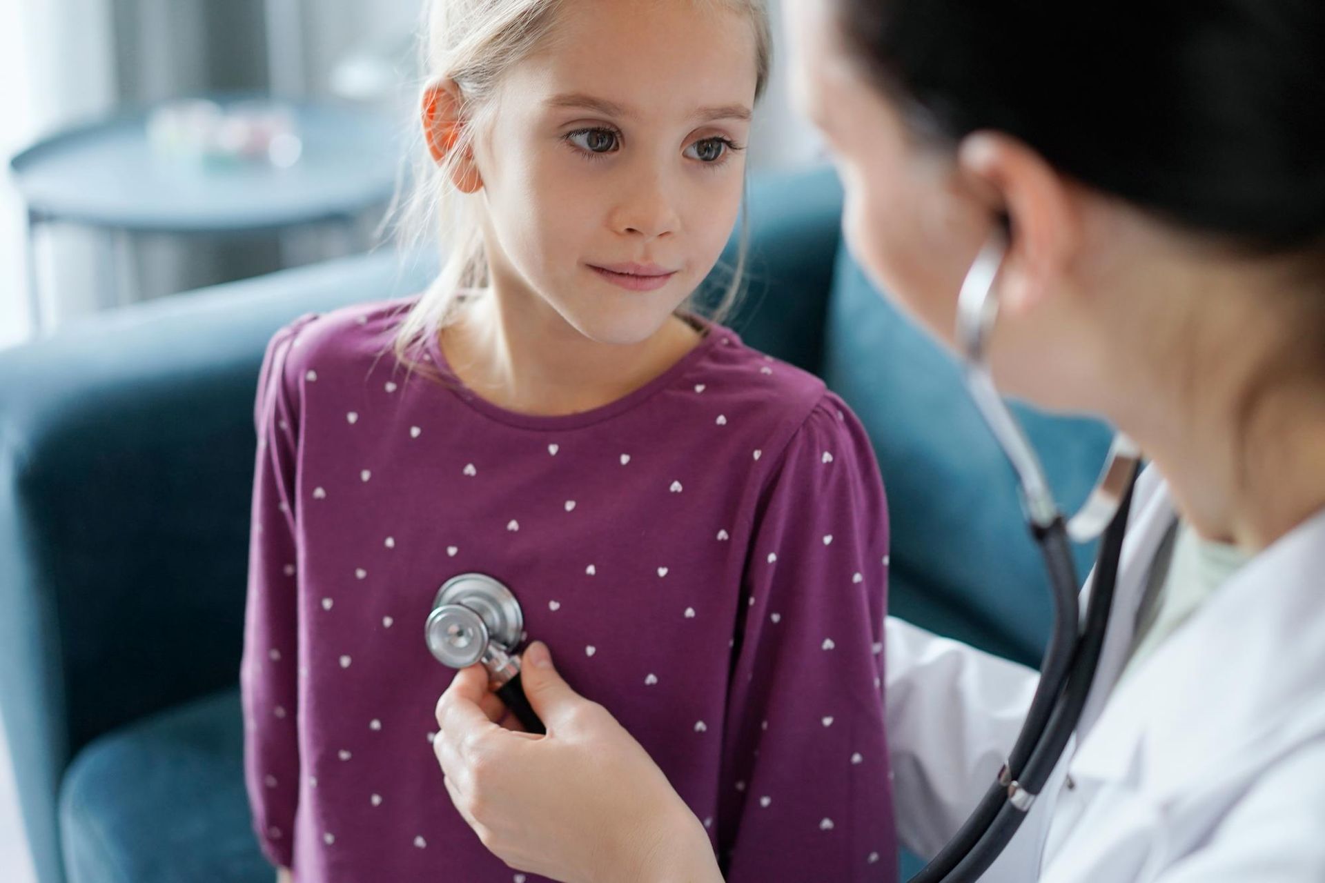 A doctor is listening to a little girl 's heart with a stethoscope.