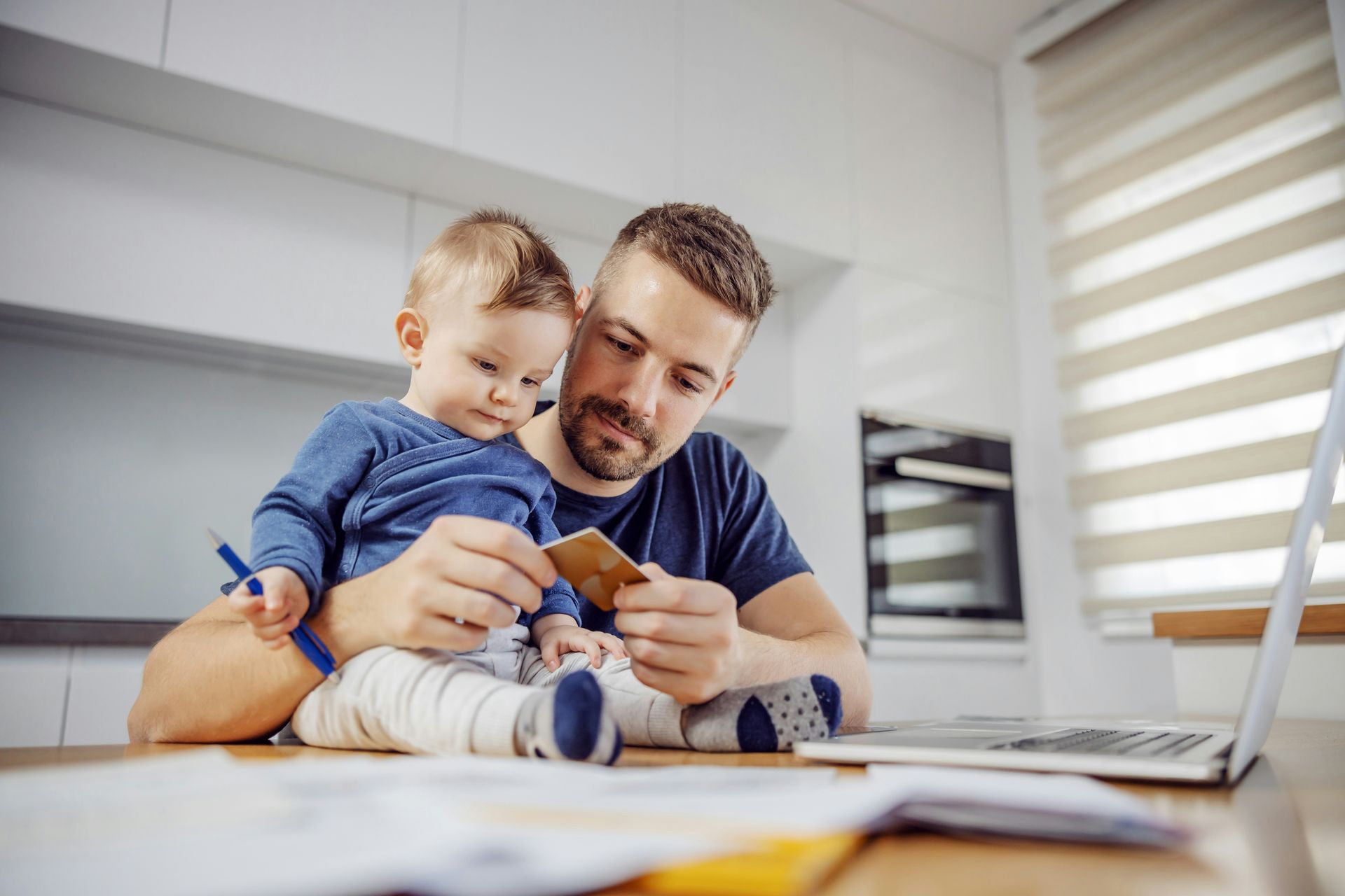 A man is holding a baby while looking at a credit card.