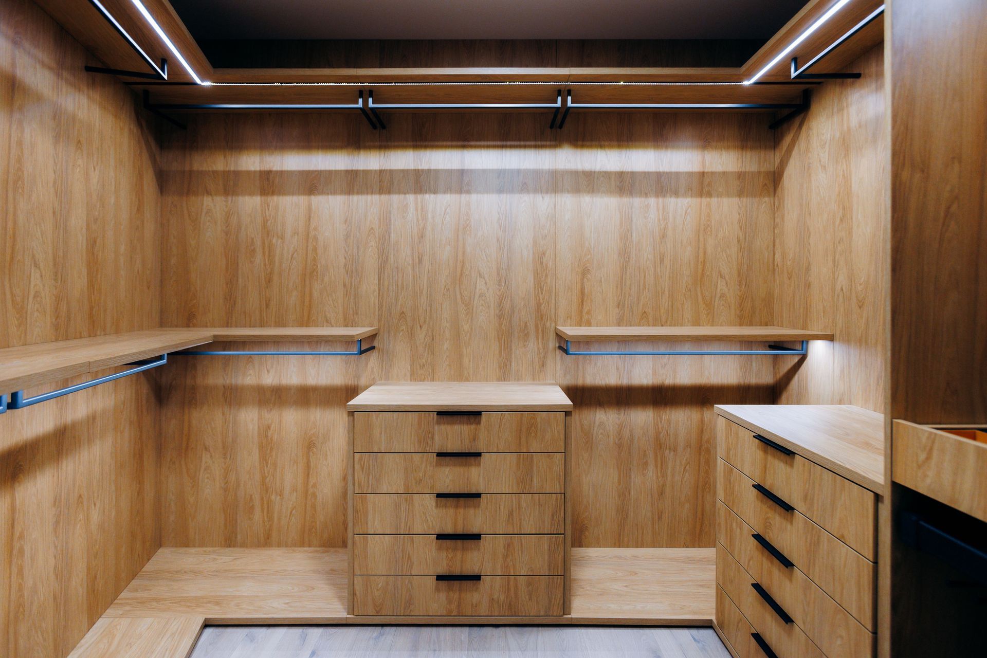 Empty wooden walk-in closet with shelves, drawers, and overhead lighting.