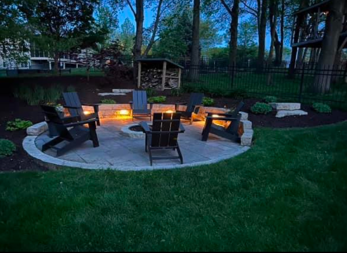 A fire pit with chairs around it in a backyard at night.