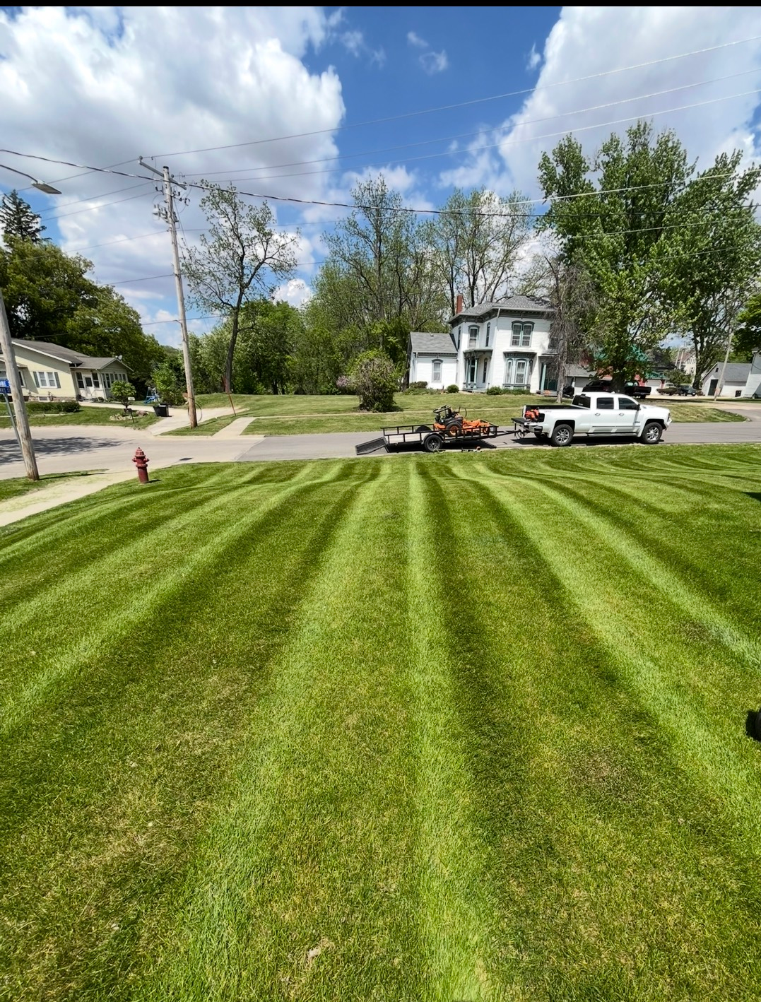 A lush green lawn is being mowed in front of a house on a sunny day.