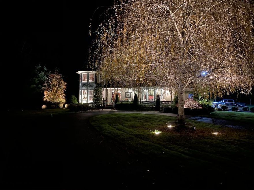 A house is lit up at night with trees in front of it.