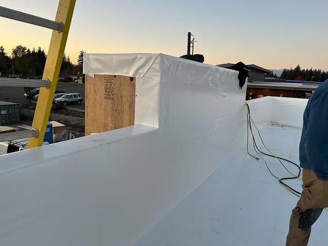 A man is standing on top of a white roof.