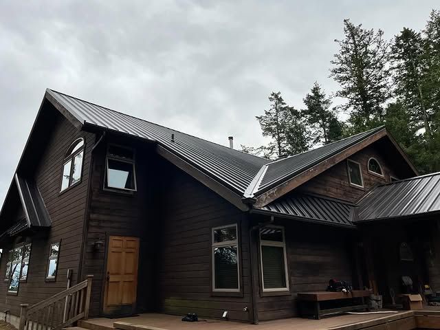 A large wooden house with a metal roof is surrounded by trees.