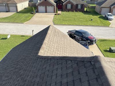 Aerial view of a suburban house roof, driveway, and a black car parked on the street.