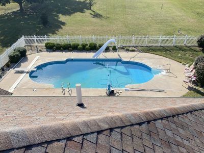 Backyard swimming pool with blue water, white fence, and patio in the foreground