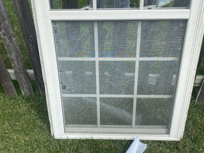 White window screen leaning against a fence in grass